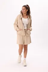 Conjunto deportivo color beige compuesto por buzo con cierre, capucha, bolsillos frontales y short con cintura elástica y cordón regulable.