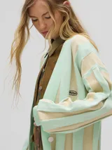 Cardigan a rayas horizontales en tonos beige y negro, de corte holgado y abierto, con botones metálicos y logo MUTMA bordado en el frente.