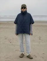 Poncho acolchado color mostaza con cuello alto y abertura frontal con cierre. Presenta un patrón capitoné de formas ovaladas y bolsillos delanteros.