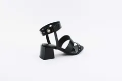 Sandalias negras de cuero con dos tiras sobre el empeine y pulsera al tobillo con ojalillos y tachas. Taco cuadrado de 5 cm.