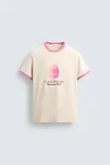 Camiseta color crema con cuello y mangas con ribete rosa. Estampado frontal de un algodón de azúcar rosa y texto "World Famous Riverland Park".