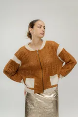 Chaqueta estilo bomber tejida color marrón con detalles en beige, cierre frontal y bolsillos delanteros.