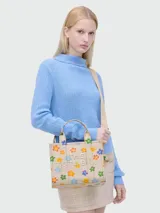 Bolso tote pequeño de lona color crema con estampado de margaritas de colores, doble asa superior y correa bandolera ajustable y extraíble.