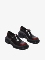 Zapato tipo Mary Jane color bordó brillante con efecto de dos tonos, suela gruesa acanalada negra y tacón cuadrado. Cuenta con una correa ajustable con hebilla sobre el empeine.