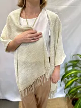 Ruana tejida color crudo con hilos dorados y flecos.