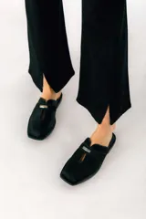 Zuecos negros de cuero con punta cuadrada y detalle de hebilla metálica plateada.