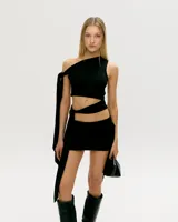 Minifalda negra con corte asimétrico, abertura en la cintura y detalle de lazo en el hombro.