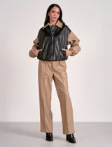Campera bomber de cuero sintético negra con mangas color beige, cuello clásico y cierre frontal con cremallera.