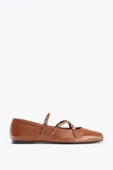 Zapato tipo bailarina color marrón de piel con acabado charol. Tiene punta cuadrada, detalle de tiras con hebillas metálicas y suela plana.