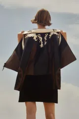 Chaqueta corta de cuero sintético color negro, marrón y blanco, con cuello de piel sintética blanca, cierre frontal con cremallera y bordado en las mangas.