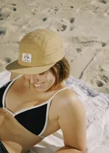 Gorra de cinco paneles color camel con logo estampado en etiqueta blanca en el frente.