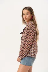 Camisa de gasa estampada traslúcida con diseño geométrico de rombos en tonos lila, naranja y negro. Tiene calce liviano y fluido, abotonado frontal y volado en la cartera.