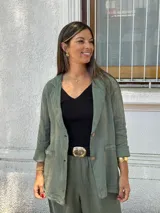 Blazer de lino color verde seco, de corte relajado y manga larga remangada. Presenta solapas anchas, cierre frontal con dos botones y bolsillos de parche.