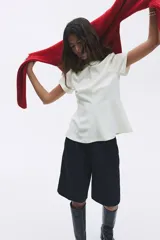 Remera blanca entallada de punto pesado interlock, con cuello redondo, mangas cortas, pinzas moldeadoras en la cintura y bajo acampanado.
