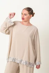 Blusa color beige con cuello redondo y mangas largas, con detalle de lentejuelas plateadas en el ruedo y los puños.