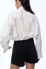 Falda pantalón de tiro alto confeccionada en denim negro. Presenta bolsillos delanteros y traseros de parche. El cierre frontal es cruzado con cremallera oculta y botón metálico.