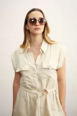 Vestido camisero corto color beige, con cuello clásico, mangas cortas con puños, dos bolsillos con solapa en el pecho, cinturón de lazo y cierre frontal con botones.