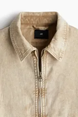 Campera color beige de sarga de algodón con efecto lavado, corte holgado, cuello clásico, cierre frontal con cremallera, bolsillos delanteros de parche, bolsillo interior con botón a presión, botones a presión ajustables en los puños y en los laterales del bajo y forro interior.