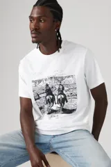Remera blanca de corte recto con cuello redondo y estampado frontal de dos jinetes cabalgando en un paisaje desértico.