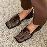 Mocasines negros de cuero con textura tipo reptil, punta cuadrada y detalle de aplique de cuero liso en el empeine.