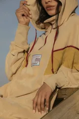 Hoodie color beige de tela de toalla con capucha, cordones rojos y apliques de tela amarilla y cinta roja en el pecho.