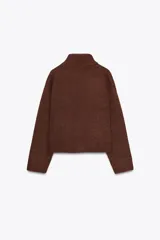 Chaqueta de punto marrón con cuello alto y manga larga. Tiene cierre frontal con botones y bolsillos de parche en el delantero.