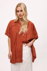 Camisa blanca de manga corta con cuello clásico, corte holgado y detalle de calado vertical en el frente.