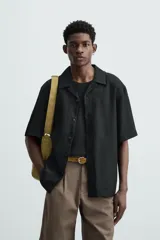 Camisa color marrón oscuro de corte relaxed fit, confeccionada en tejido de lino. Tiene cuello bowling, manga corta, bajo con aberturas laterales y cierre frontal de botonadura.
