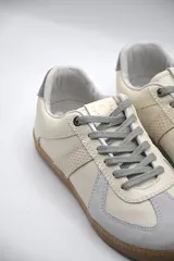 Zapatillas urbanas de cuero color crema con detalles en gris y suela de goma marrón.