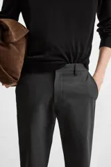 Pantalón negro de corte slim fit, confeccionado en tejido elástico. Cuenta con cintura elástica, bolsillos frontales y traseros de vivo. Cierre frontal con cremallera y botón.