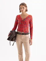 Top de punto color rojo con estampado de labios en azul y fucsia. Presenta escote en V profundo con jareta ajustable para anudar, mangas largas y calce al cuerpo.