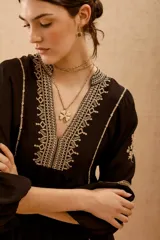 Vestido corto negro con bordado de hilo blanco, escote en V y mangas largas abullonadas.