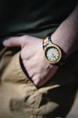 Reloj de pulsera con caja y esfera de madera clara, malla de madera oscura con incrustaciones de madera clara.