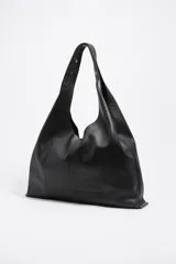 Bolso de hombro tipo hobo de tamaño maxi, confeccionado en piel vacuna negra, con estructura blanda y asa de hombro ajustable con remaches metálicos. Presenta el logo metálico de BIMBA Y LOLA en la parte inferior frontal.