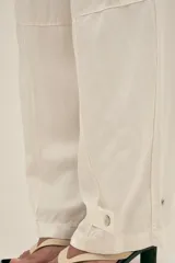 Pantalón color crema de lino y tencel, con bolsillos laterales, cintura elástica y cordón ajustable. Detalle regulable en el tobillo.