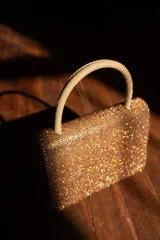 Cartera de mano dorada cubierta de strass, con forma rectangular y asa rígida.