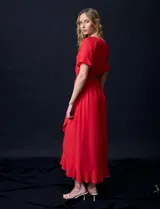 Vestido largo de gasa color rojo, con escote en V, mangas cortas con volados, cintura elastizada con lazo de ajuste y ruedo asimétrico con volados. Tiene forro interno a tono.