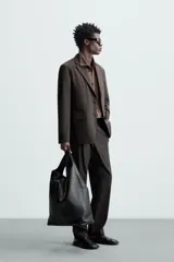 Blazer negro de corte relaxed fit, confeccionado en tejido de algodón con acabado ligeramente encerado. Tiene cuello con solapas de muesca, manga larga con puños abotonados, bolsillo de vivo en el pecho, bolsillos de solapa en la cadera, bolsillo interior, aberturas en la espalda y cierre frontal con botones.