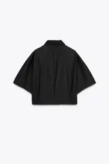 Camisa negra de popelín con cuello solapa y manga ancha por debajo del codo. Detalle de pinzas en la espalda y cierre frontal con botones ocultos por solapa.