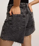 Short de jean estilo mom, color negro con efecto marmoleado (acid wash). Presenta tiro alto, trabillas para cinturón, cierre tradicional, bolsillos y ruedo cortado sin remate.