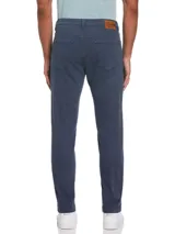 Pantalón azul de gabardina con cinco bolsillos, cierre y botón en la cintura. Tiene remaches metálicos en los bolsillos y aplique de cuero con logo en la parte trasera. Calce slim taper fit, más holgado en cadera y muslos, afinándose hacia el tobillo.