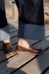 Mocasines de cuero marrón con diseño de cocodrilo, suela plana y detalle de antifaz en el empeine.