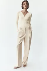 Pantalón de vestir color crema, de tiro alto y pernera ancha, con pinzas delanteras, bolsillos frontales y falsos bolsillos de doble vivo en la espalda.