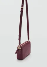 Bolso bandolera rectangular color borgoña con textura granulada, cierre de cremallera, asa larga regulable y logo MNG en dorado.