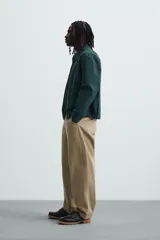 Pantalón color caqui de corte amplio, con pinzas en la cintura, bolsillos laterales y traseros con botón.