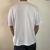 Remera blanca de corte oversize con cuello redondo y estampado pequeño en el centro del pecho con el símbolo del yin yang rodeado de llamas amarillas y naranjas.