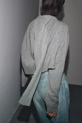 Chaqueta de punto color rosa pálido, con cuello redondo y cierre frontal de botones oscuros. Presenta mangas largas y un corte a la cintura.