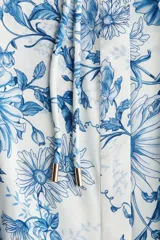 Vestido largo blanco con estampado floral en tonos azules. Tiene cuello mao, botones ocultos en la parte delantera, mangas largas abullonadas con puños elásticos, cinturón fino extraíble y costura fruncida debajo de la cadera para dar vuelo.