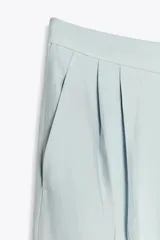 Pantalón de tiro medio color celeste confeccionado en hilatura con mezcla de lyocell. Tiene bolsillos laterales, pinzas delanteras, pierna ancha y cierre frontal con cremallera y botón.
