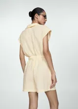 Mono color crema de lino, con cuello camisero, manga corta, cintura elástica con lazo, cierre frontal con botones y bolsillos de parche delanteros.